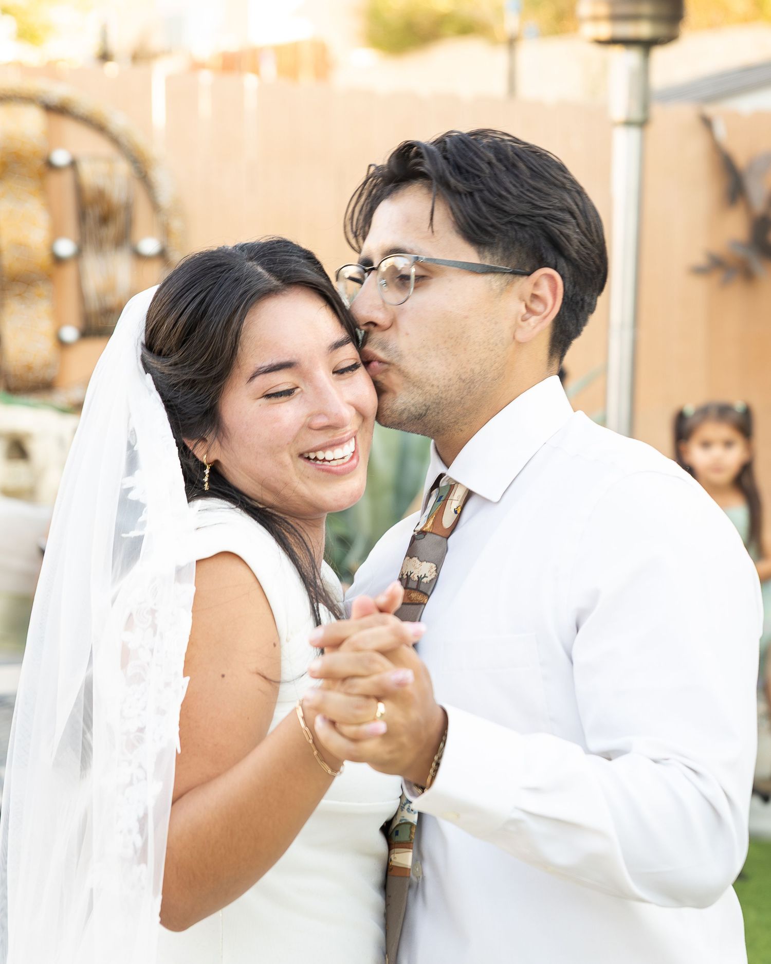 The newlywed couple dances as the groom kisses his bride. A professional photographer captures a moment in a candid photo as bride smiles.
