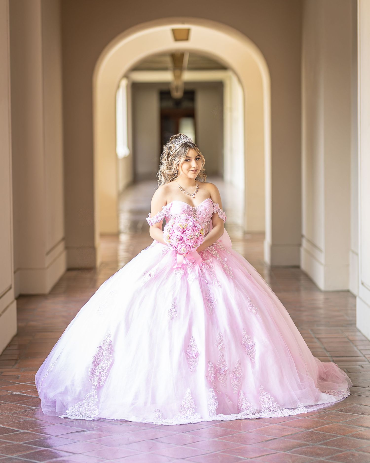 Quinceañera wears an elegant pink dress and poses using natural lighting. Professional photographer uses 85mm lens to photograph model.