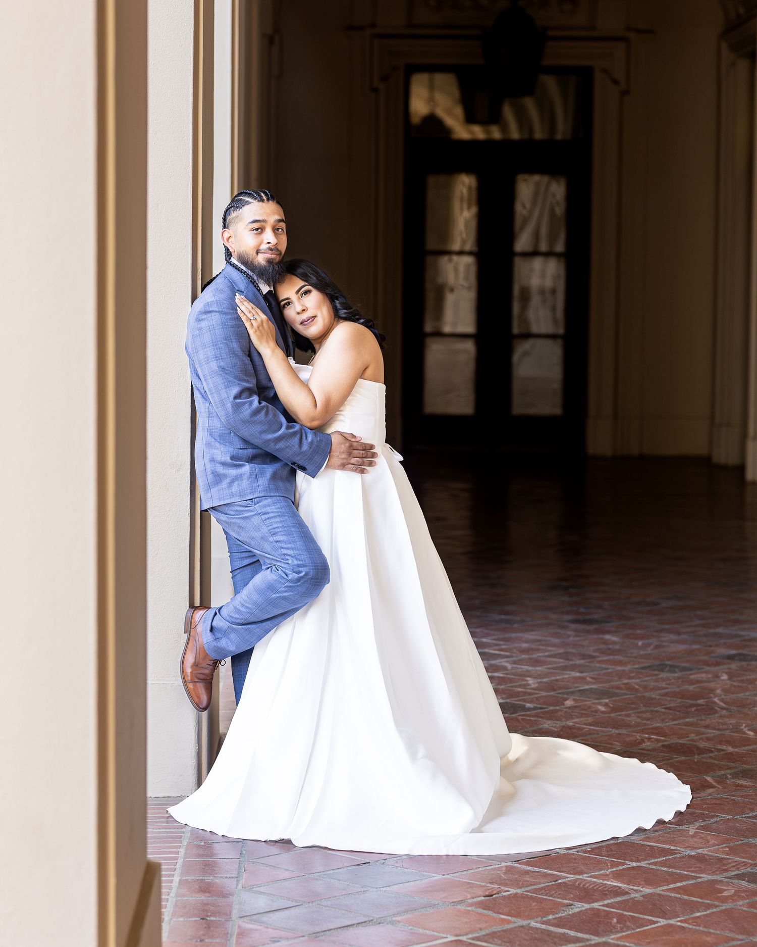 Wedding couple embraces during romantic portrait session in arched courtyard with terracotta tile floors.