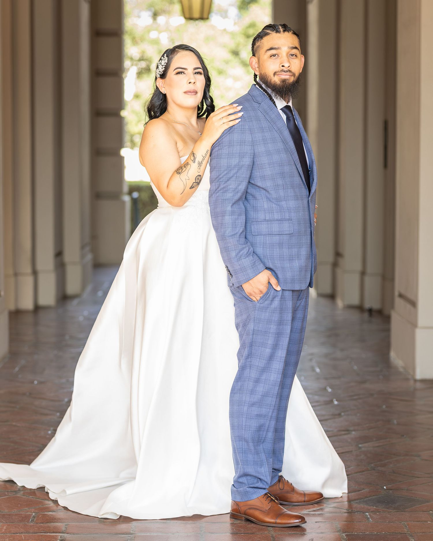 The bride and groom share romantic glances while walking together down an elegant covered walkway with arched columns.