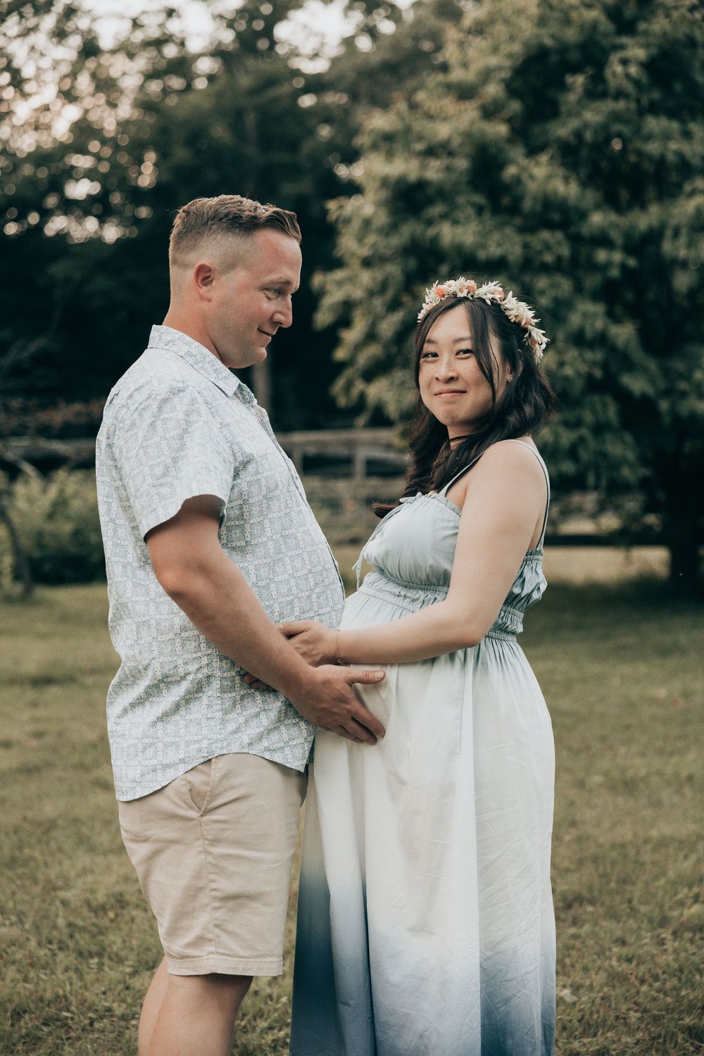 A couple embraces in a grassy field during a romantic photoshoot wearing coordinated white and beige outfits.