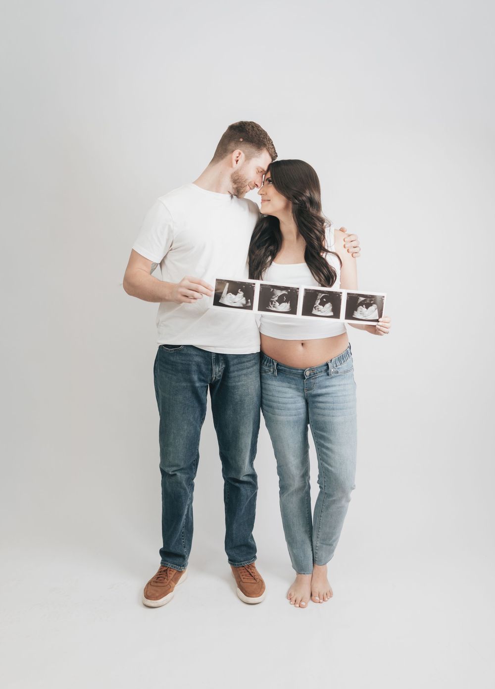 Couple holding ultrasound photos together, touching foreheads, celebrating pregnancy milestone.