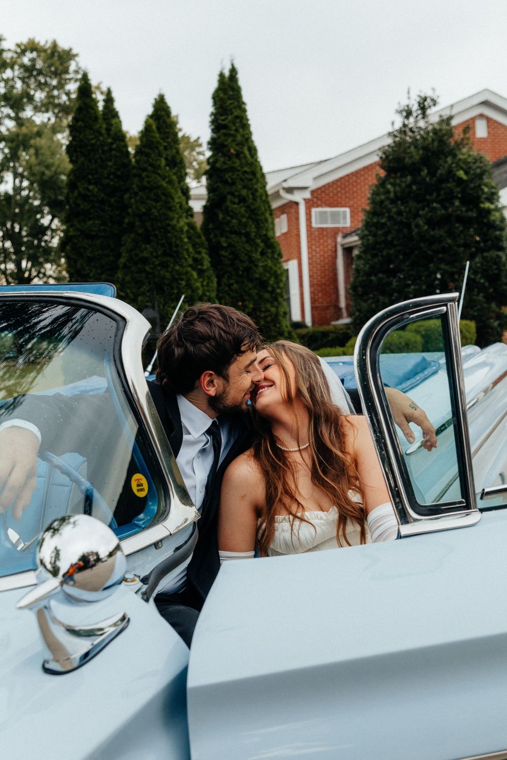 A romantic moment captured in a vintage blue car during a wedding celebration.