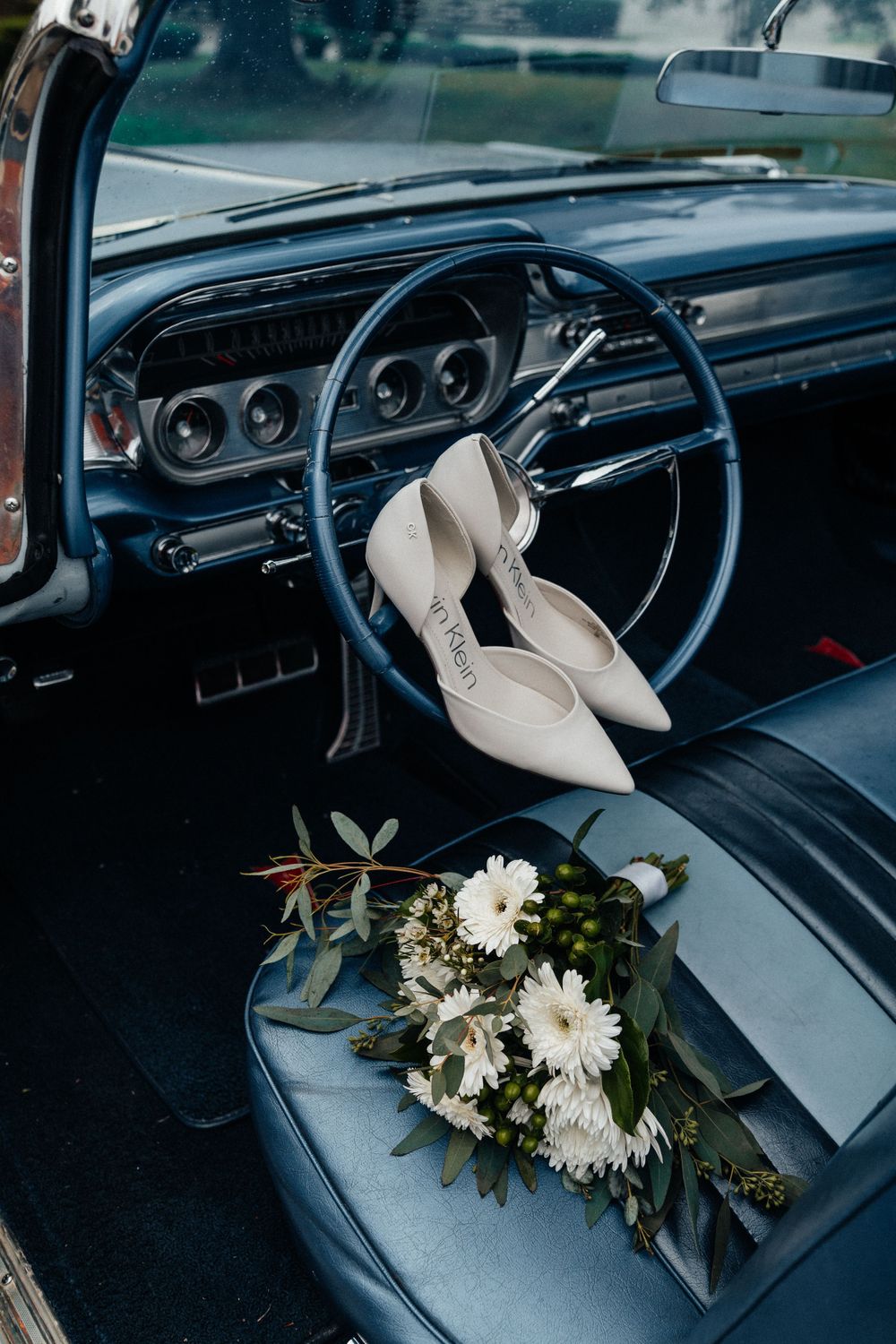 White floral bouquet rests on gray vintage car seat with classic dashboard in view.