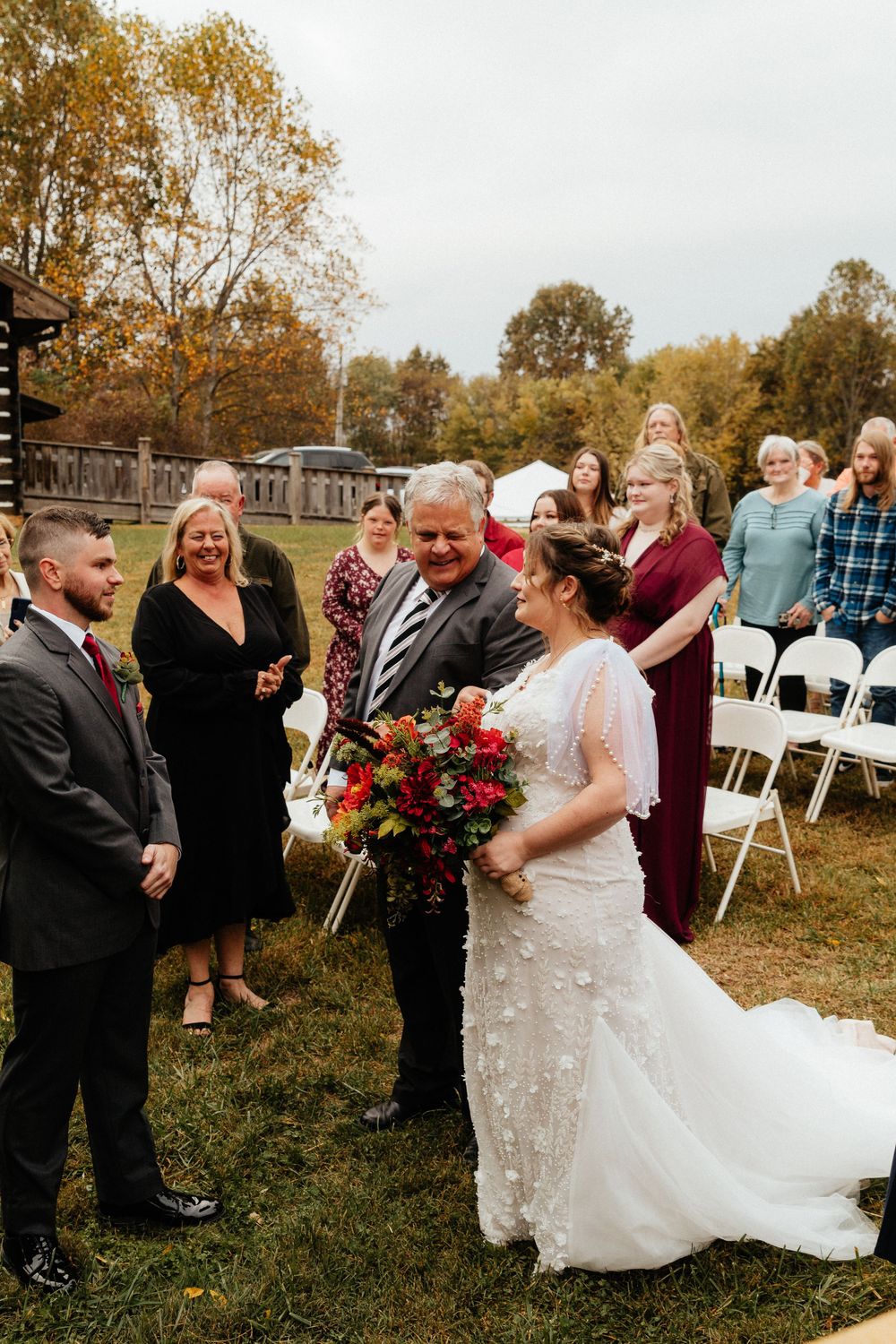 Wedding guests celebrate during an outdoor autumn reception with white chairs.