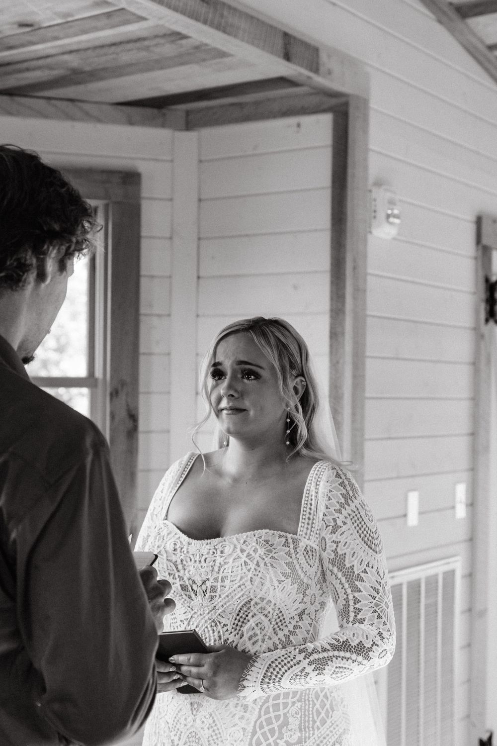 A detailed white lace wedding dress is showcased in an indoor setting with natural lighting.