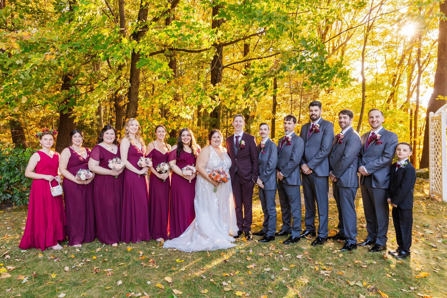 Wedding party in burgundy and navy poses together against golden fall foliage.