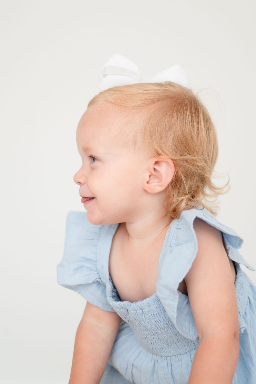 Side profile of a child with blonde hair wearing a light blue dress against a white background.