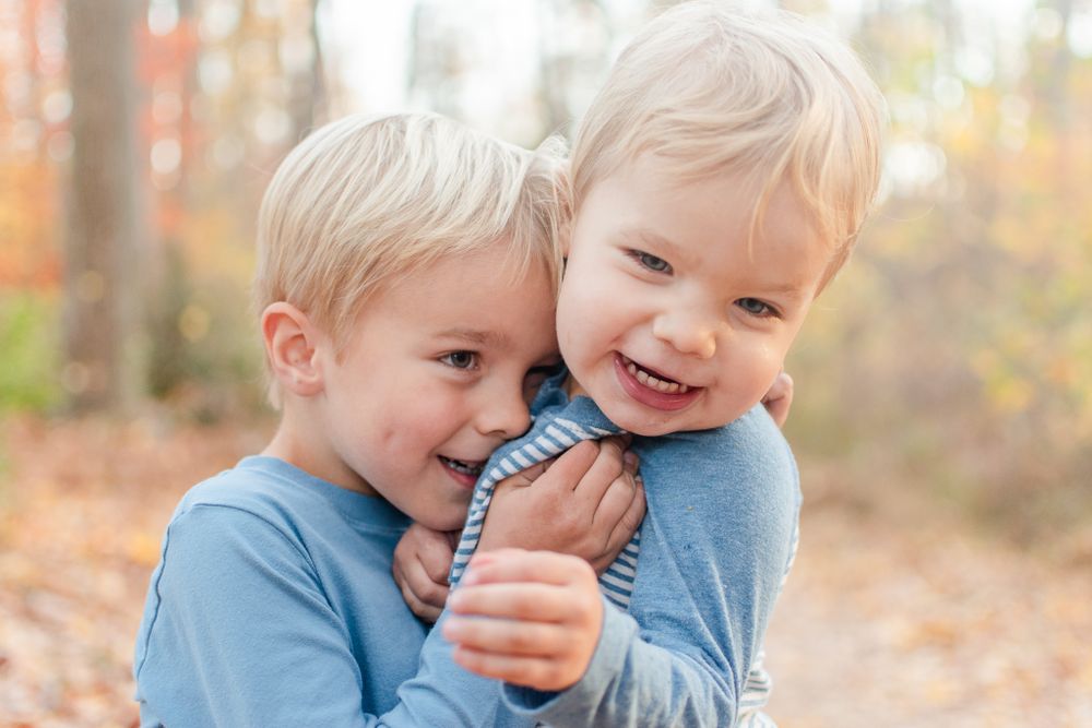 Two young children share a joyful moment together among fall leaves.