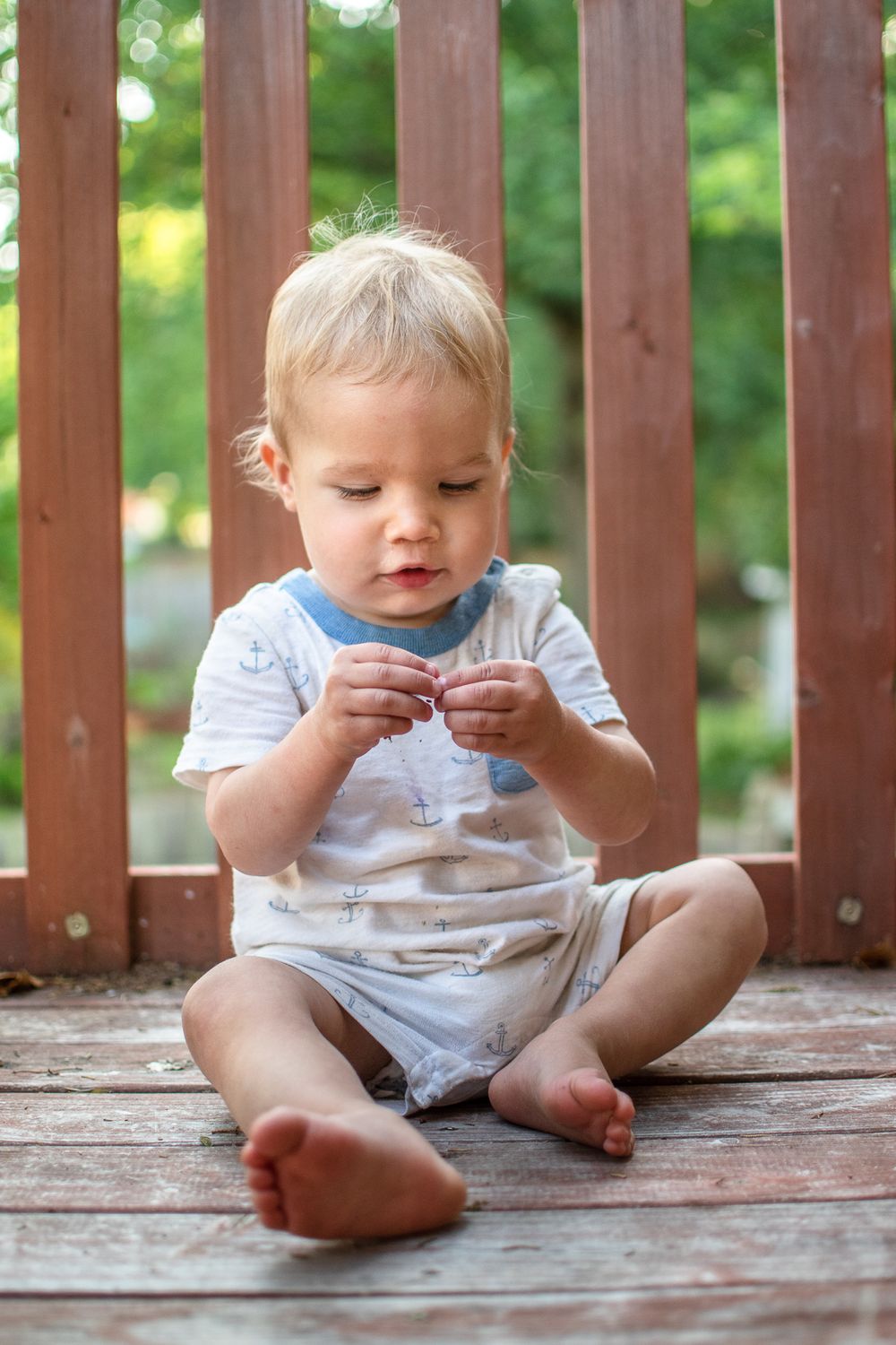 Small child sitting cross-legged on wooden deck examining something in hands.