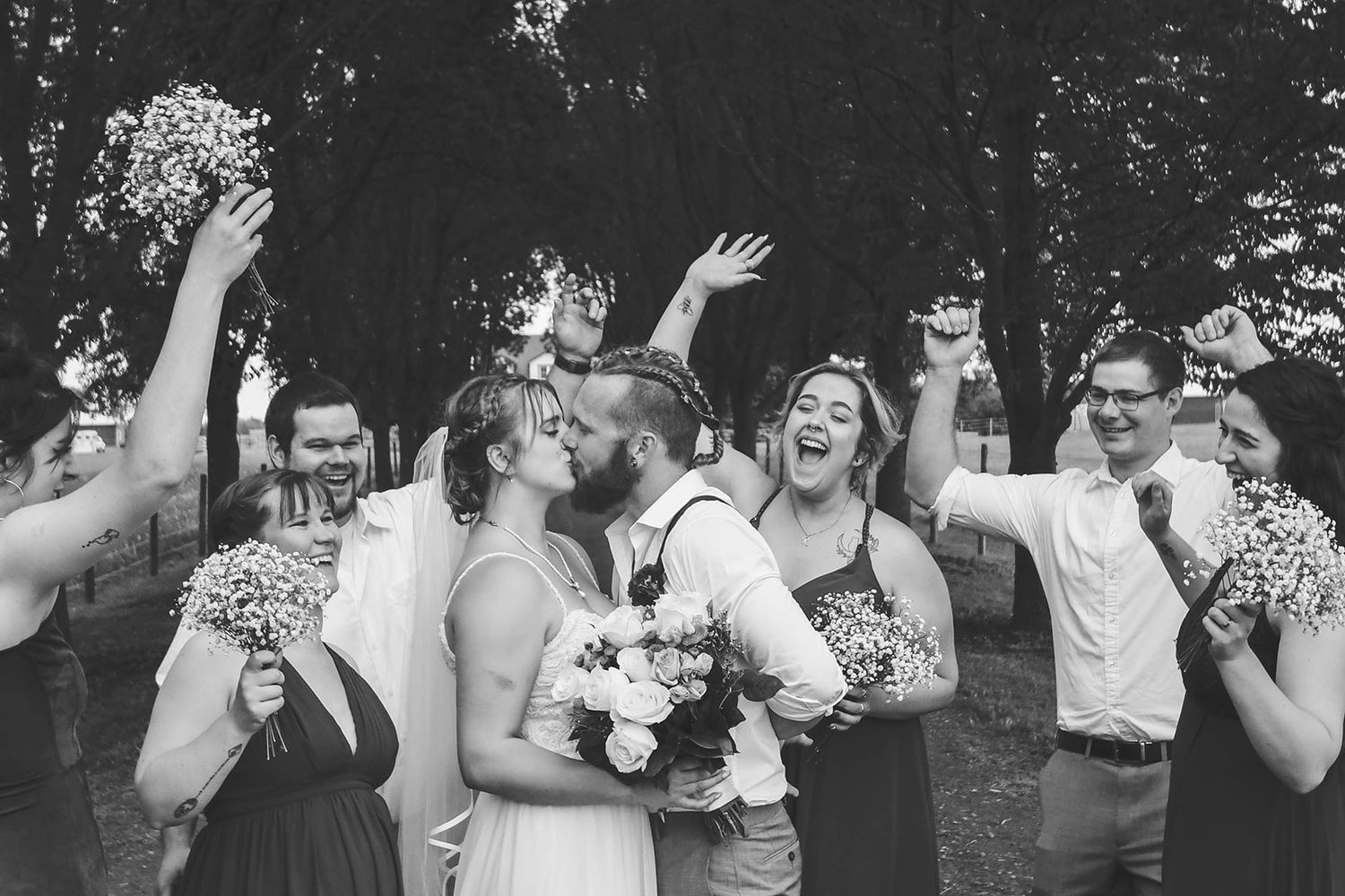 Joyful wedding party celebrates with laughter and raised arms in black and white photography.