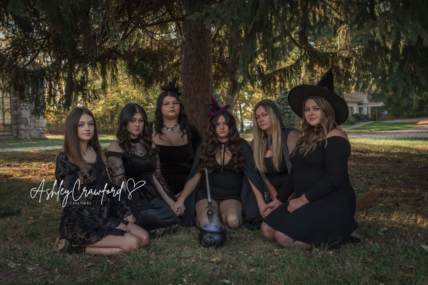 Gothic-styled group sits on grass with a cauldron for dark autumn photoshoot.