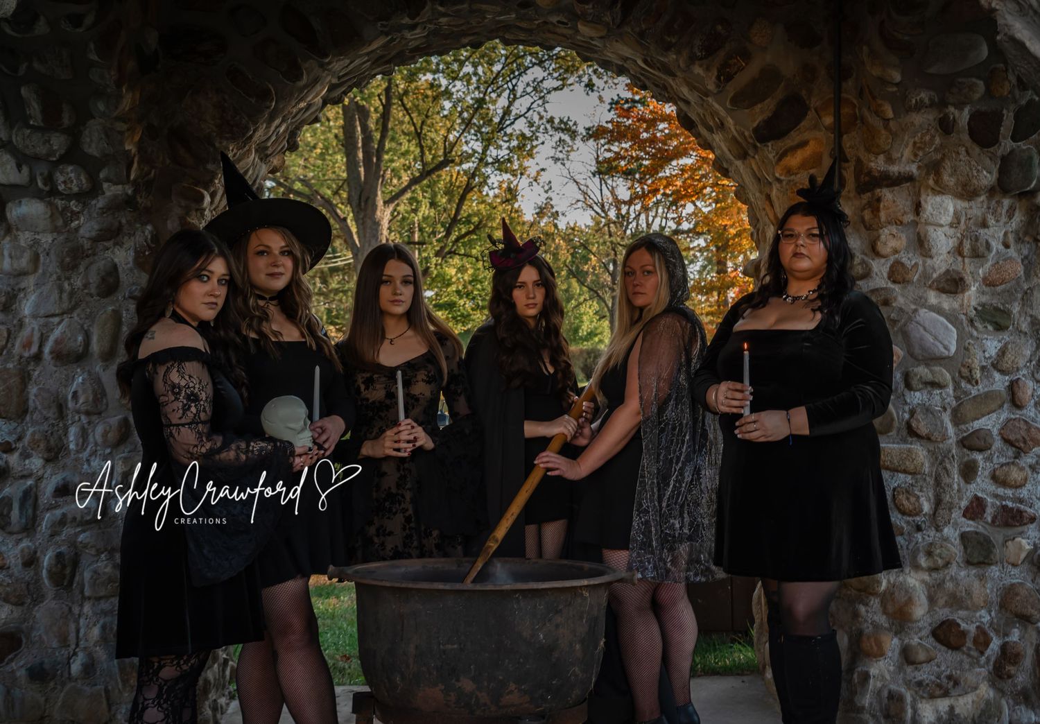 Witchy group photo with black dresses and a cauldron under a stone arch.