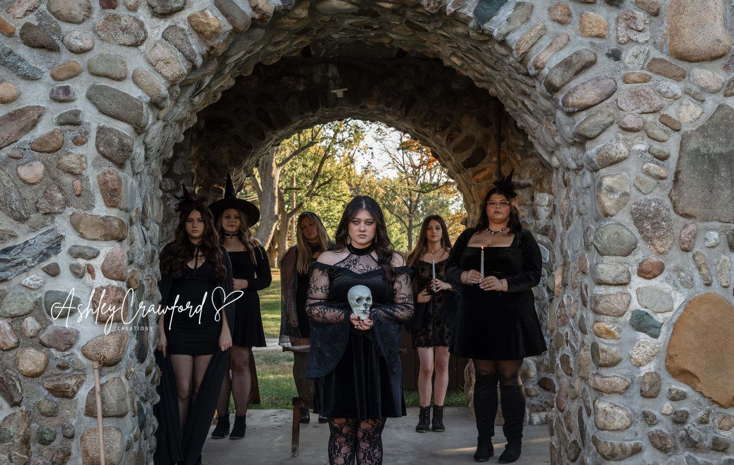 A group in gothic attire poses under a stone archway during an autumn photoshoot.