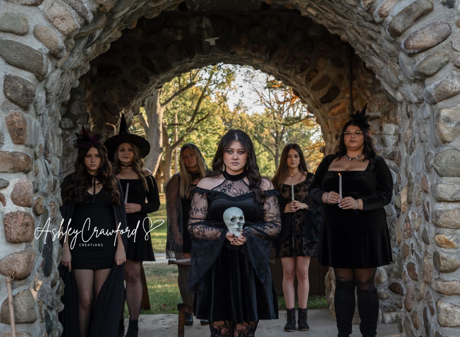 Group dressed in dark gothic clothing poses for a moody autumn photo under stone architecture.