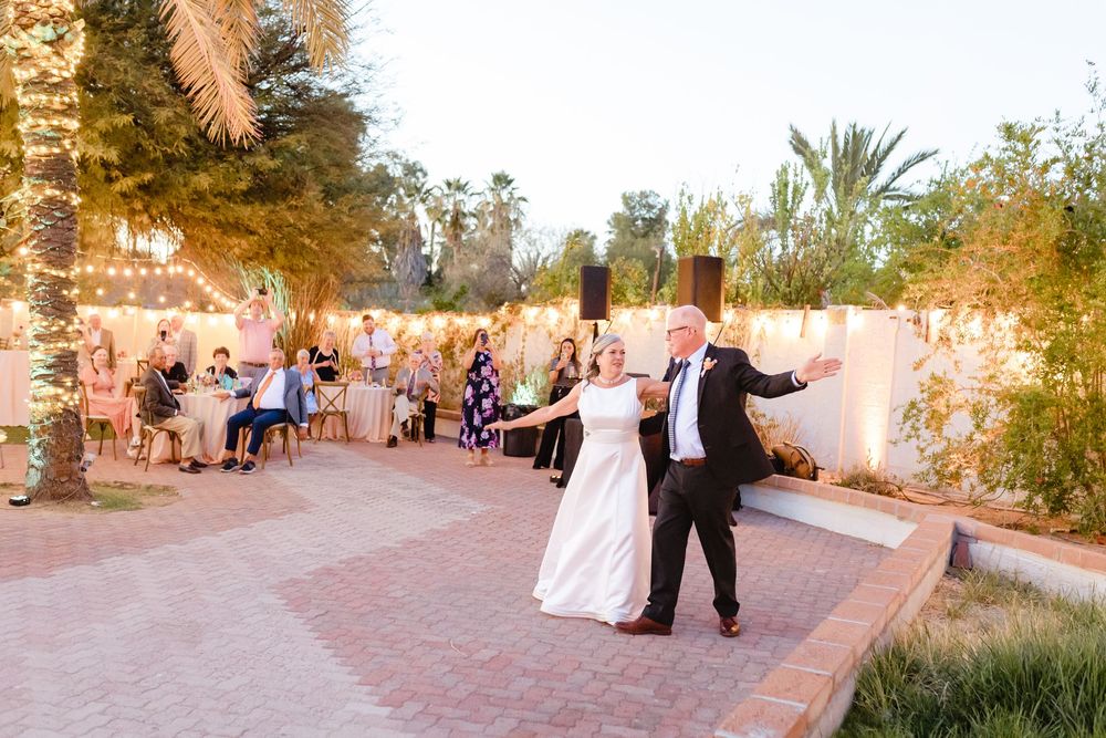 A couple dances together at an outdoor evening wedding reception with string lights and guests watching from tables.