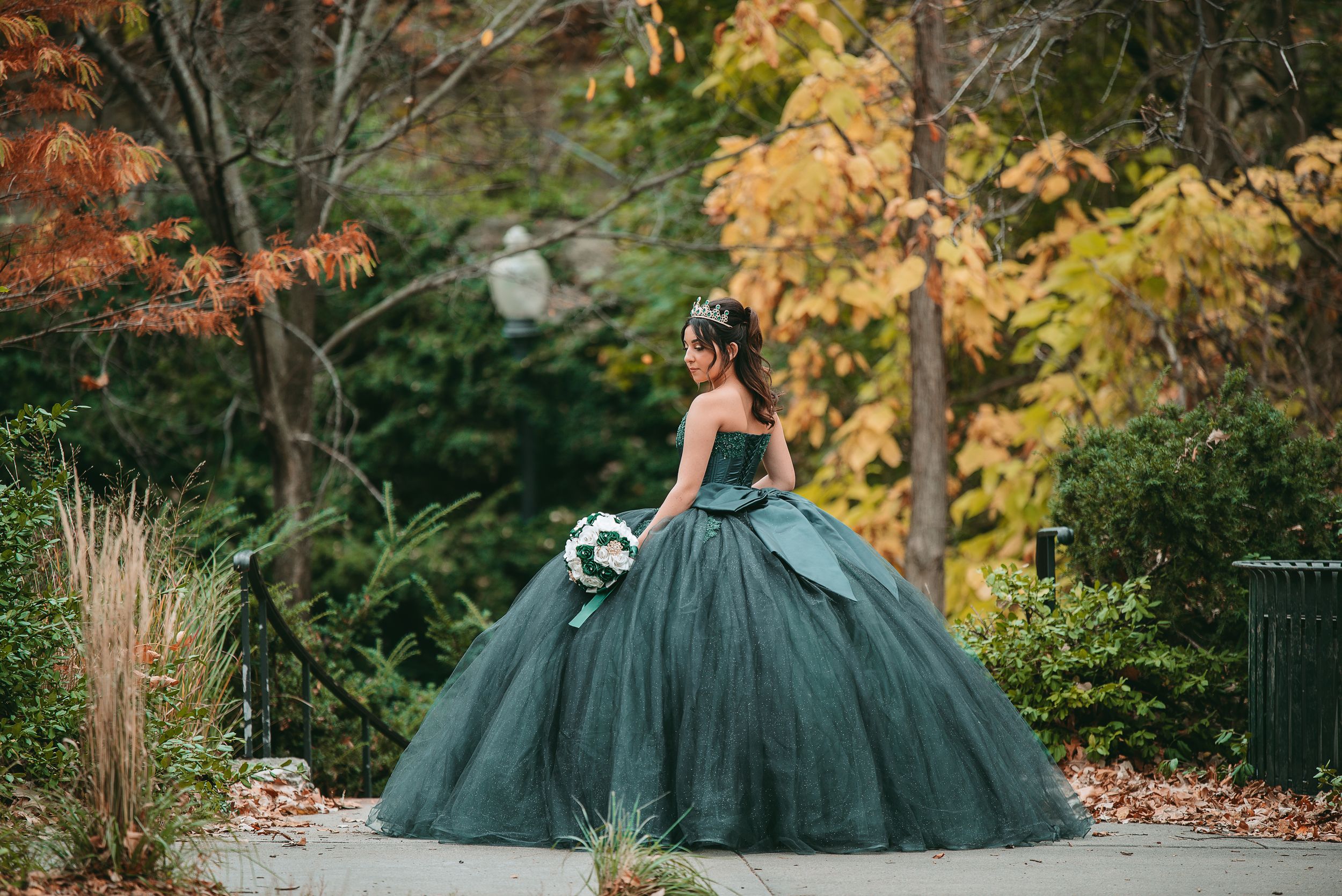 Dark green formal gown with full tulle skirt photographed against autumn foliage.