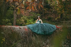Forest green quinceañera dress photographed on stone steps surrounded by autumn leaves.