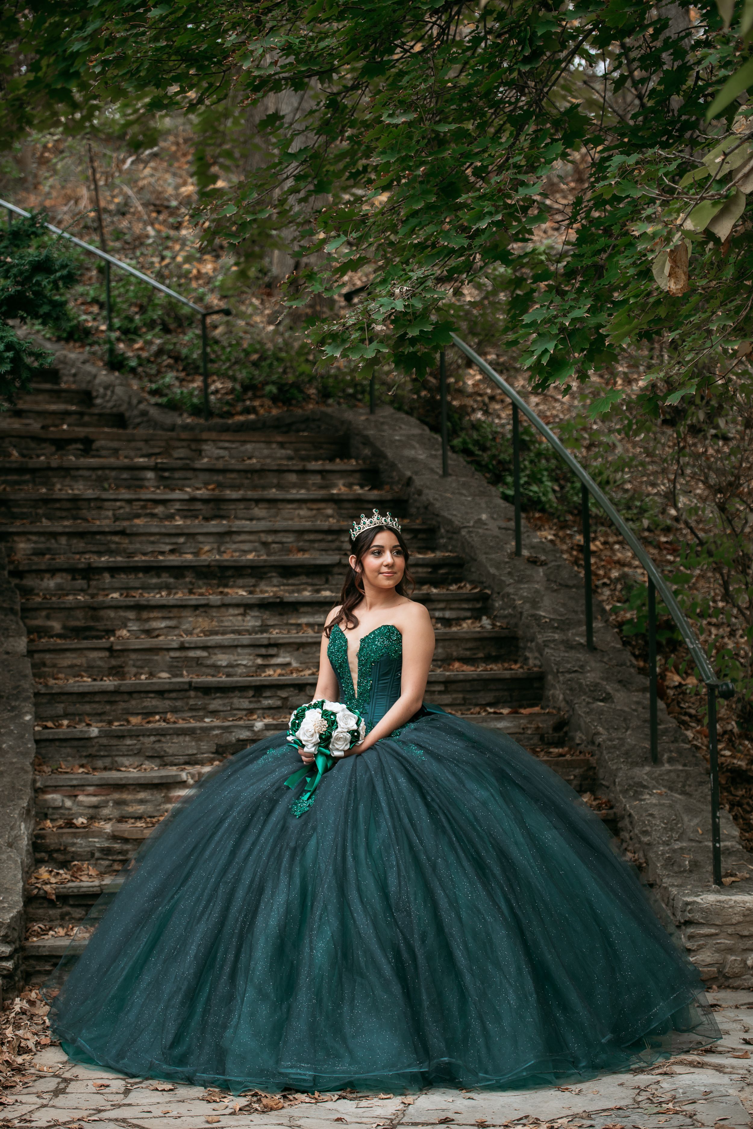 Emerald green ball gown showcased on rustic stone steps in an outdoor setting.