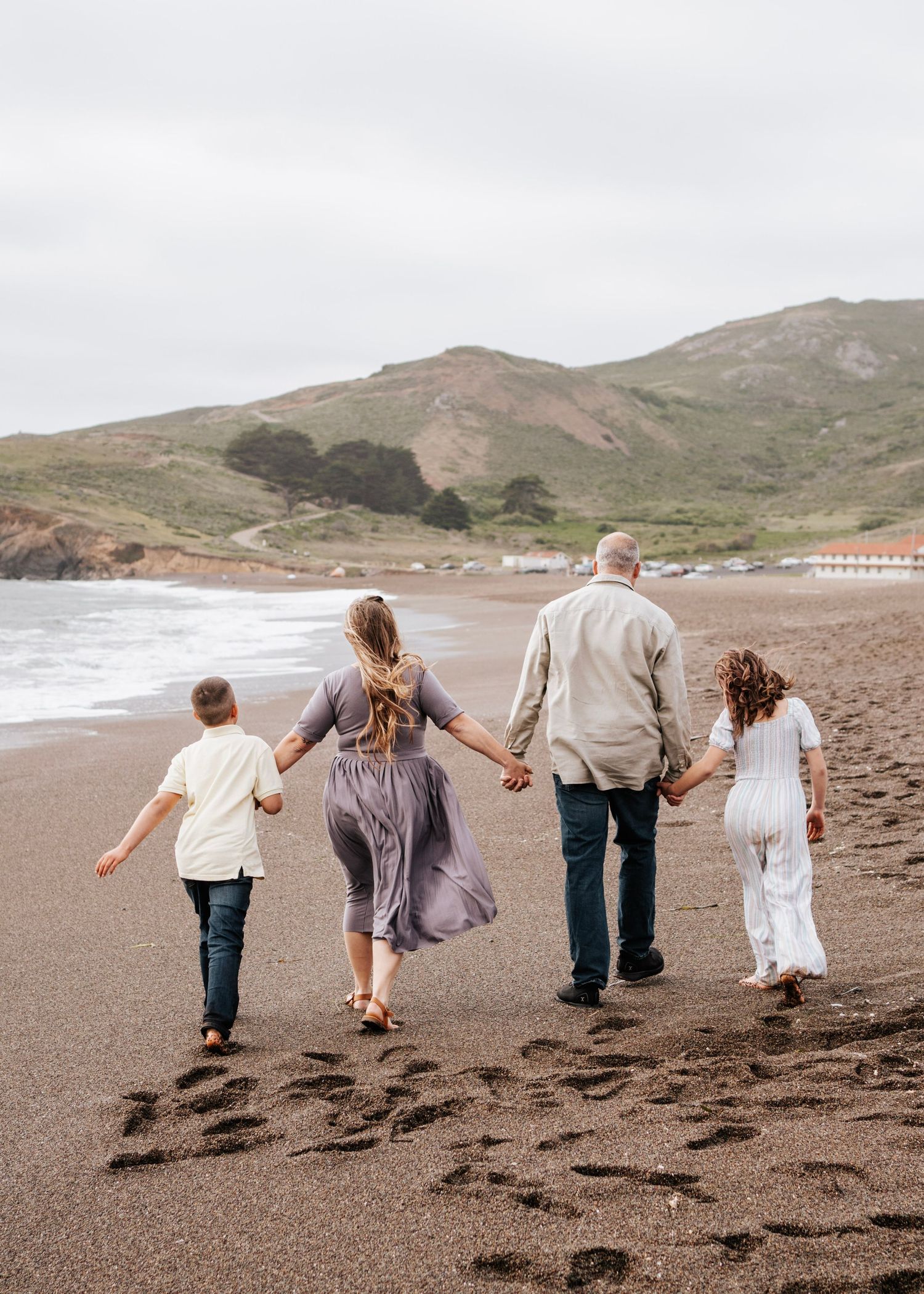 A family of four walks away from the photographer on the beach