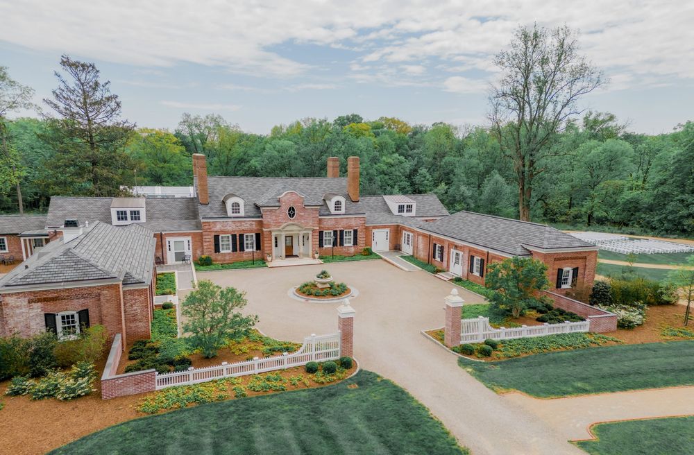Aerial view of luxurious red brick Georgian estate with circular driveway and manicured landscaping.