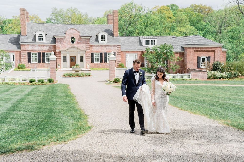 A couple walking together on a gravel path leading to an elegant brick Georgian-style mansion with manicured lawns.