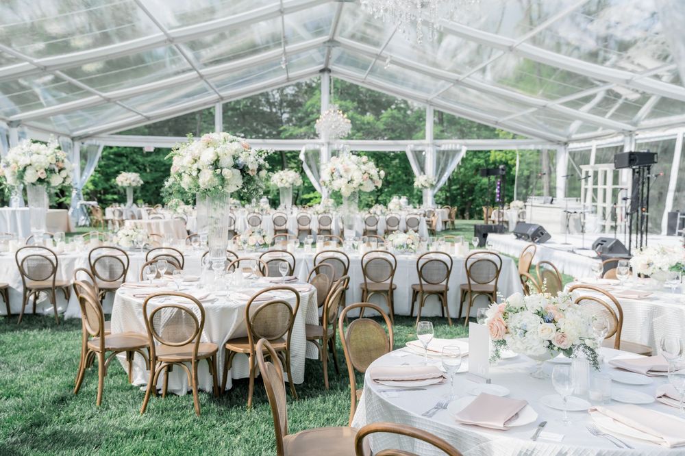 Elegant wedding reception setup with round tables, white florals and clear tent creating an airy garden atmosphere.