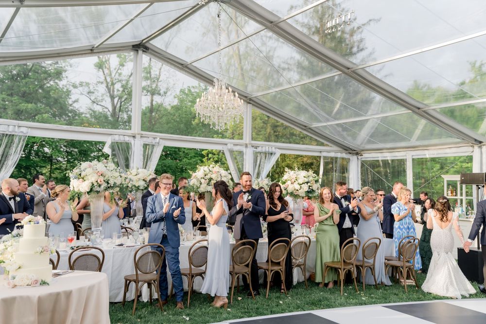 Guests celebrate under an elegant clear-top tent with tables beautifully set for an outdoor wedding reception.