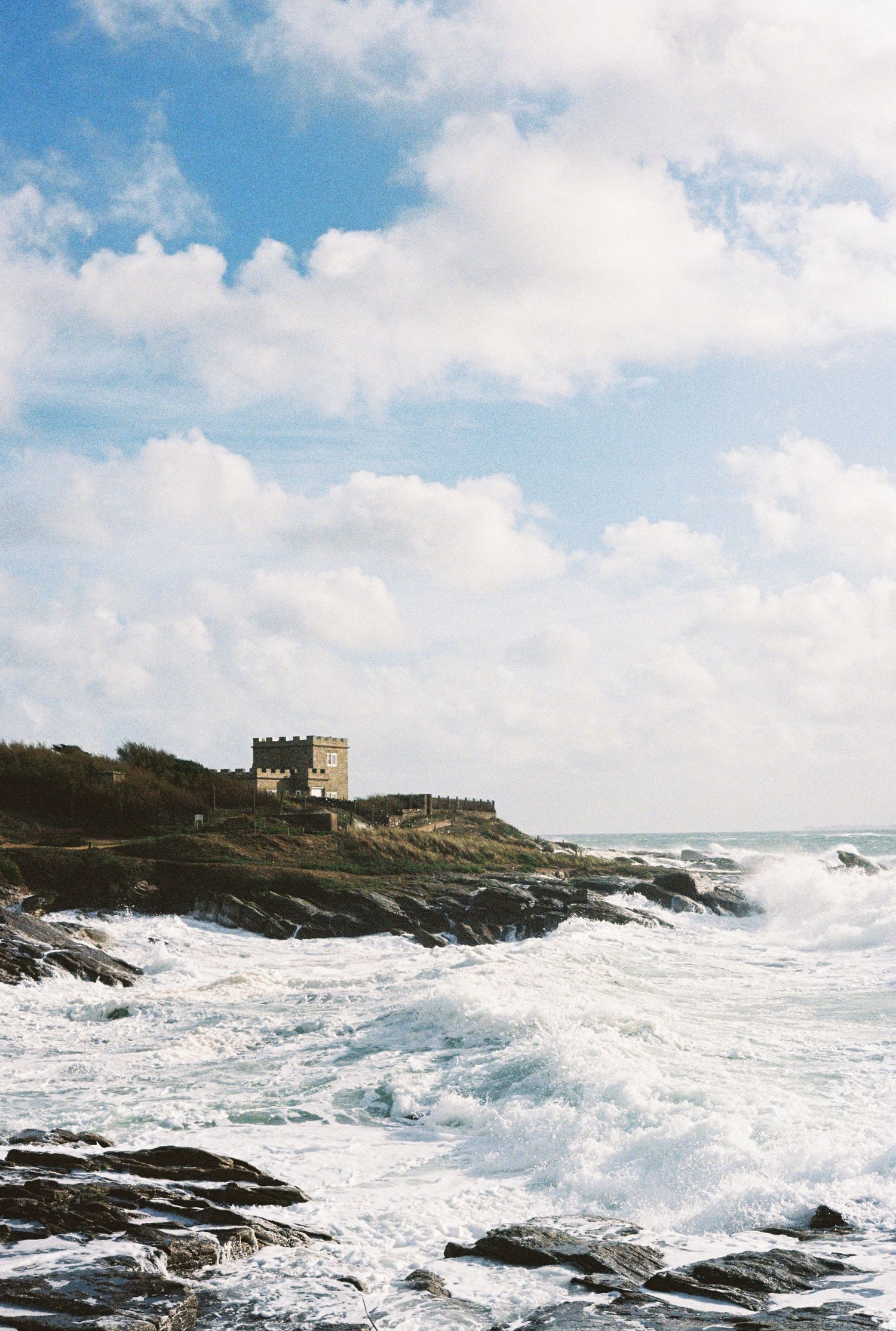 Stone fortress perched on rocky coastal cliffs with dramatic crashing waves below.