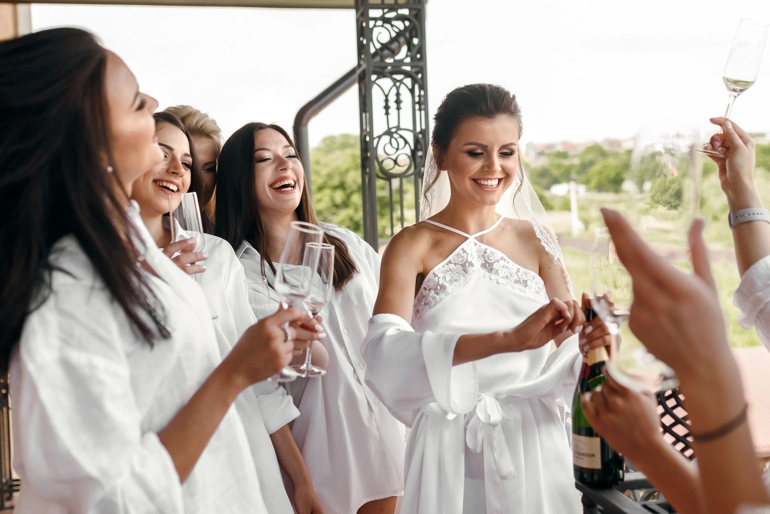 Group in white robes celebrating with champagne glasses on a balcony.