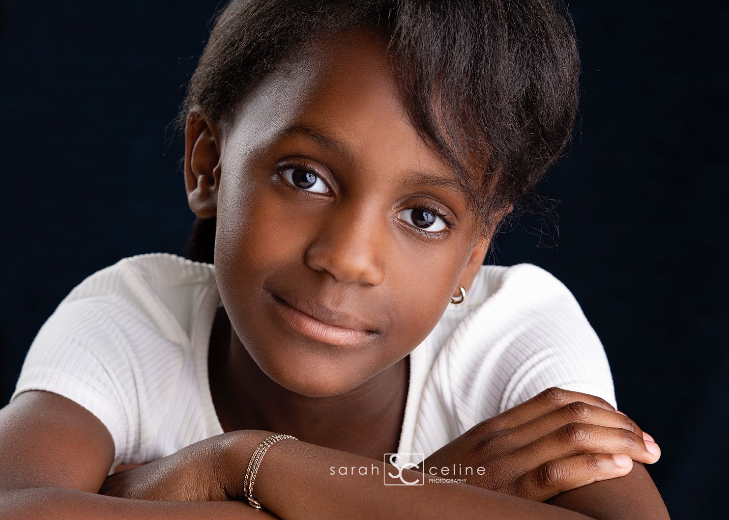 A portrait photograph against a black background featuring a warm smile and white t-shirt.