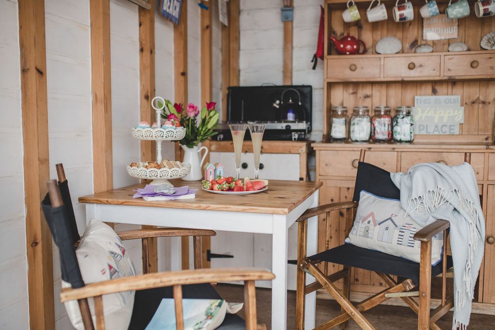 Cozy rustic dining nook with wooden table, chairs and shelving displaying glassware and home decor accessories.