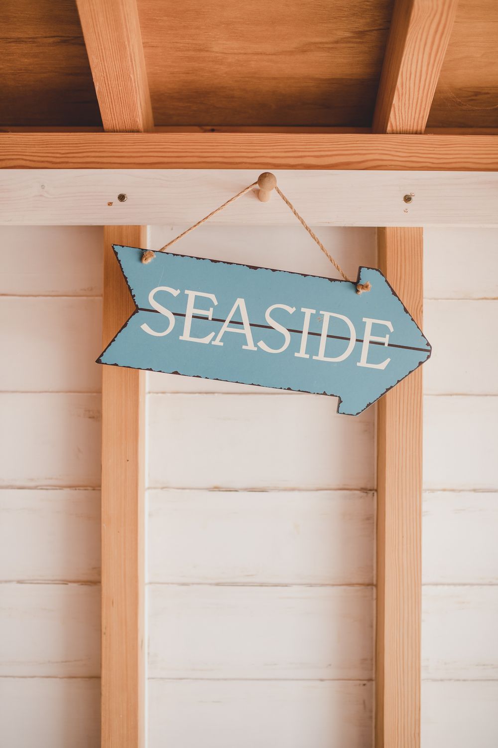 A distressed blue wooden arrow sign reading 'SEASIDE' hanging on a white plank wall.
