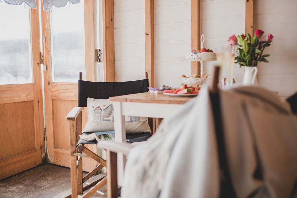 A cozy dining nook with wooden doors, white table, and pink flowers in a vase by a window.