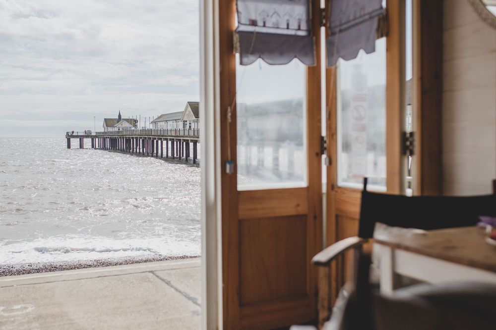 Looking out through an open wooden door at a misty coastal pier stretching into the ocean.