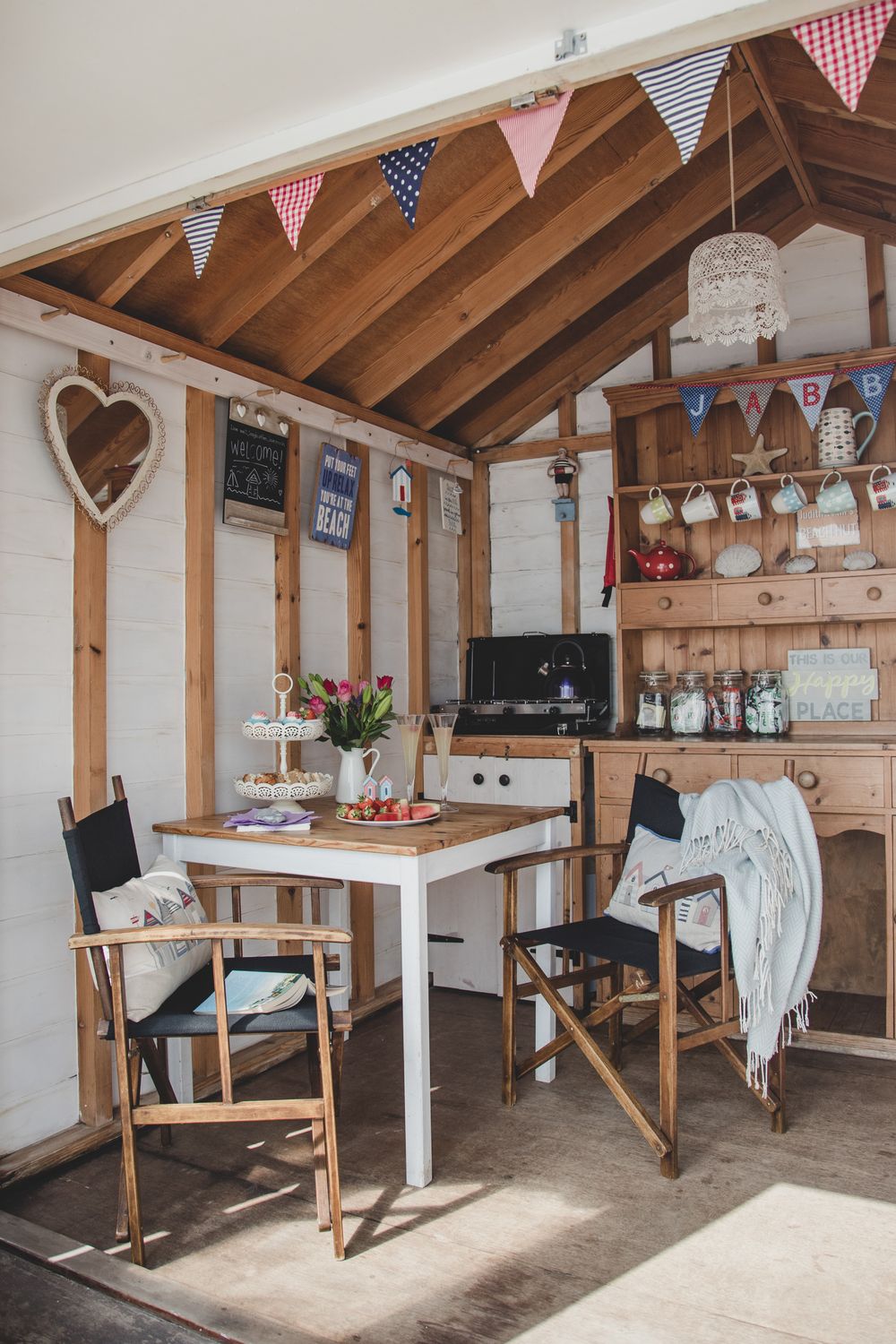 Cozy cabin interior with white table, directors chairs, bunting flags, and rustic wooden decor creating a charming atmosphere.