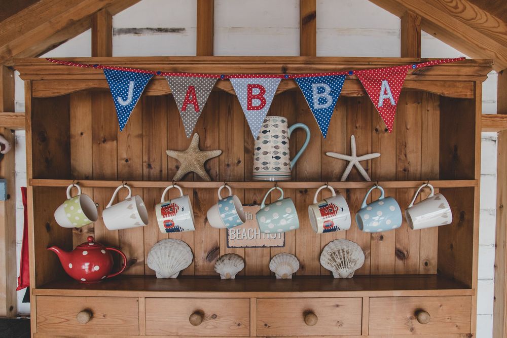Rustic wooden shelf decorated with colorful JBBBA bunting banner, starfish decor, and hanging teacups.