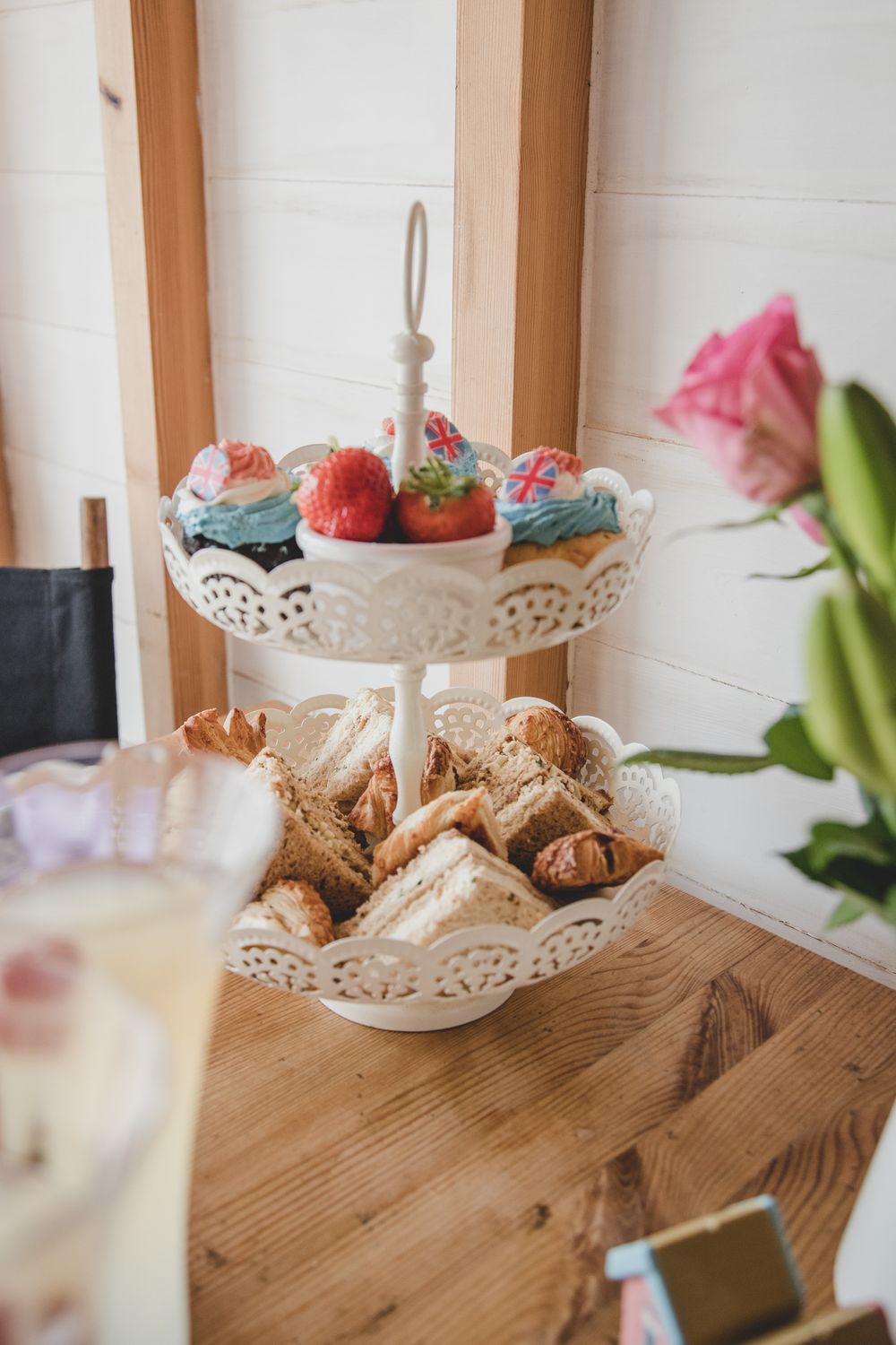 A white tiered dessert stand displays blue frosted cupcakes and strawberries on top with pastries on the bottom level.