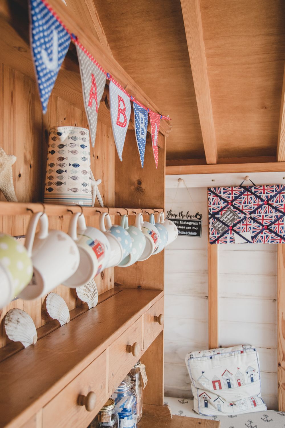 A cozy rustic shelf displays white teacups and bunting flags with a decorative geometric pattern in the background.