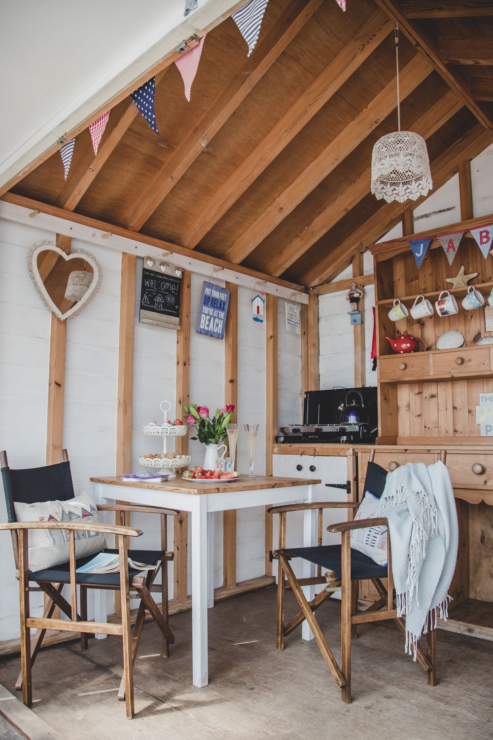 Cozy beach house interior with white table, director chairs, bunting flags, and rustic wood accents in summer cottage style.