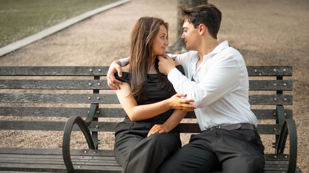 Romantic couple sitting close together on a park bench wearing black and white formal attire.