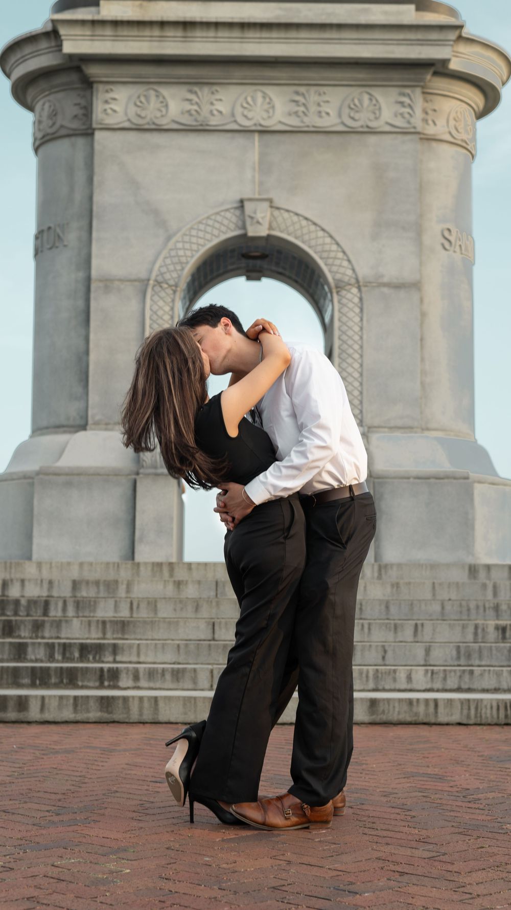 A romantic embrace between a couple in front of a grand stone monument with ornate architectural details.