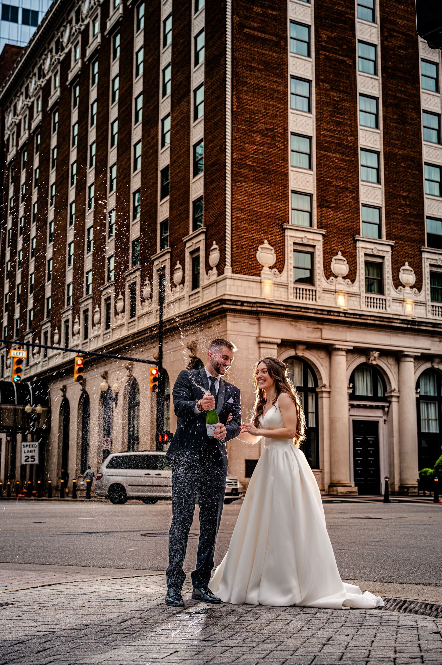 A wedding couple stands together on a cobblestone street in front of a grand historic building with ornate architecture Grand Rapids