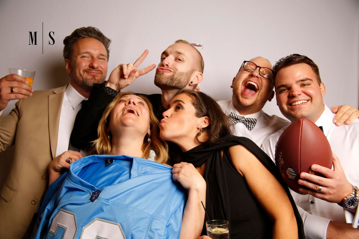 Group wearing sunglasses and hats pose together for fun photo booth portrait.