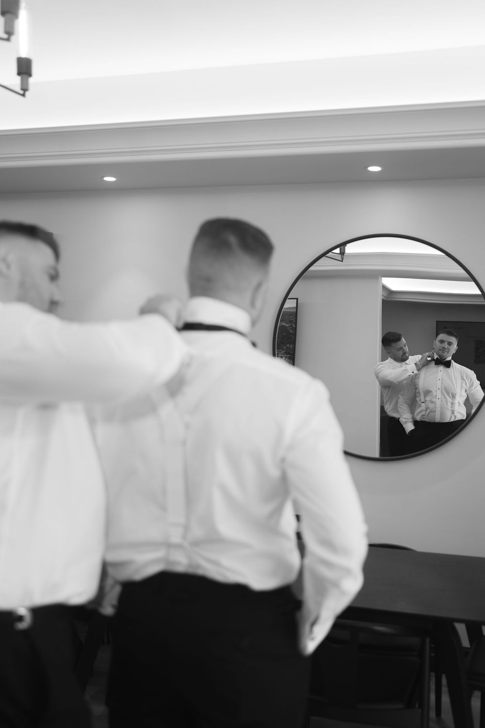 Stylish black and white reflection of men getting ready in a round mirror mounted on a wall.