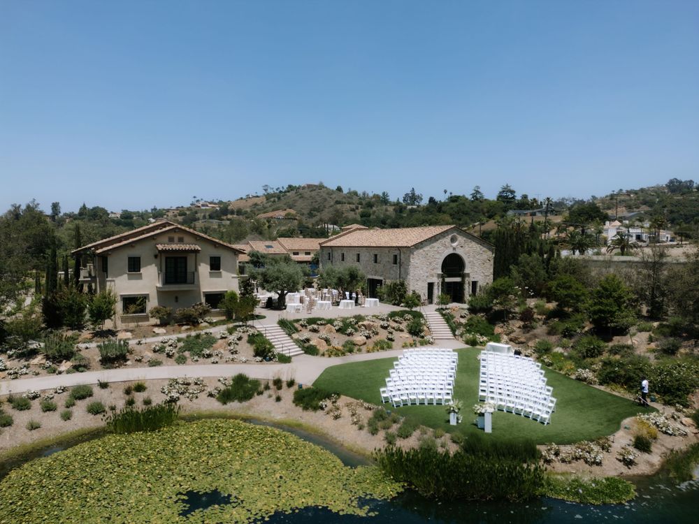 Aerial view of luxury estate with white event seating setup on manicured lawn surrounded by Mediterranean landscaping.