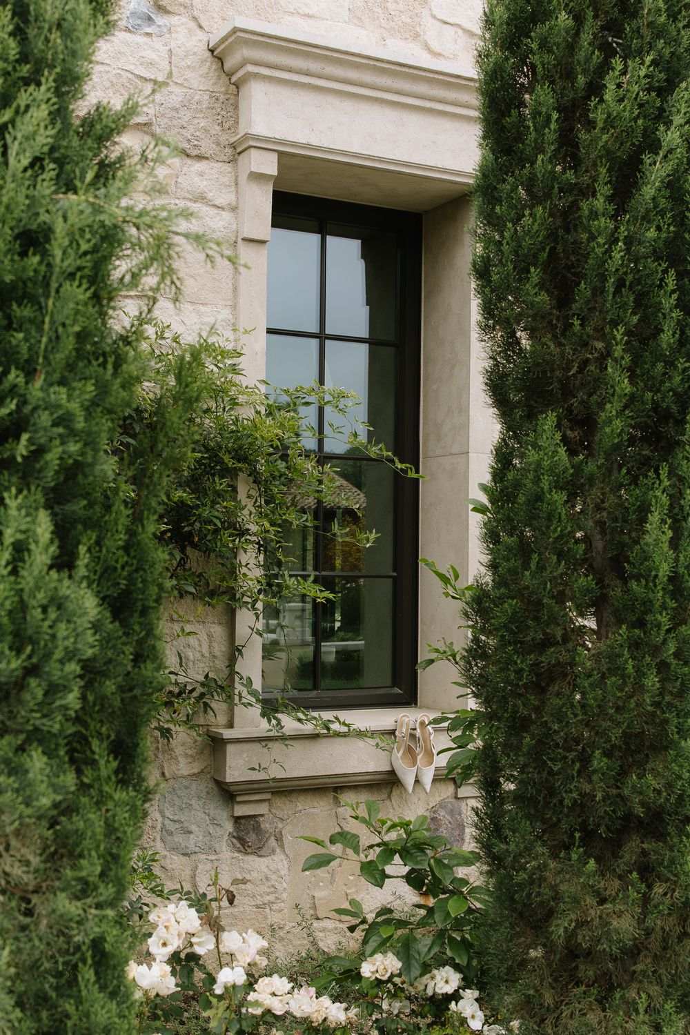 Stone window frame with climbing roses and cypress trees at luxury venue.