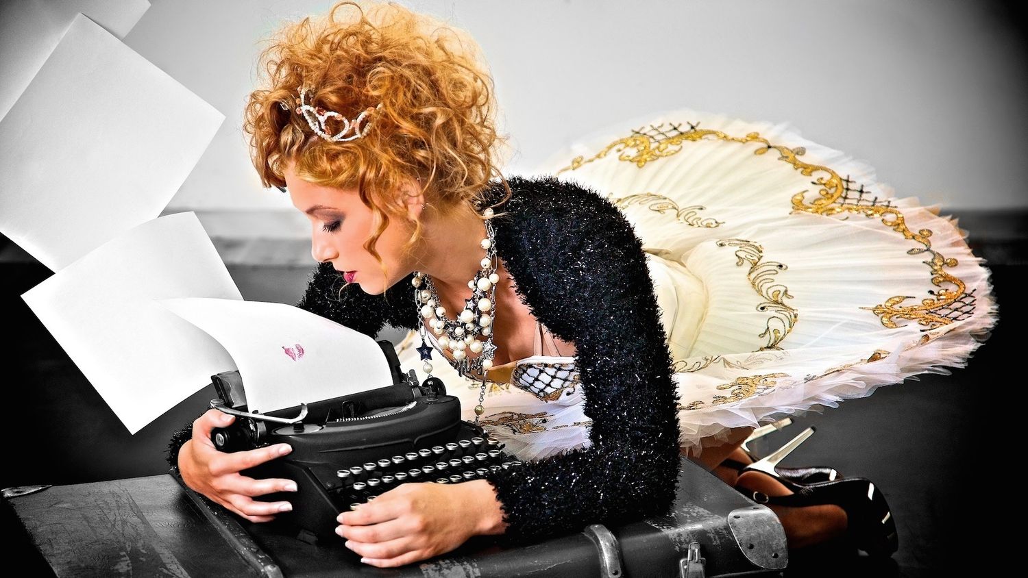 A retro-style scene of someone in a black sequined top and cream dress using a vintage typewriter on a desk.