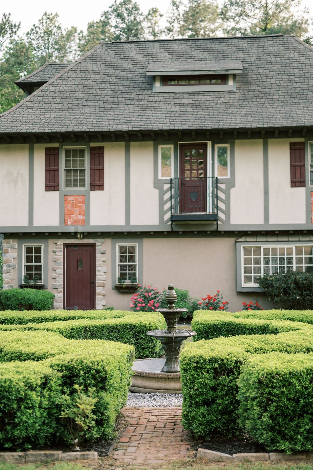 Tudor style house with manicured hedge garden and ornate fountain features brick pathway and distinctive architectural details.