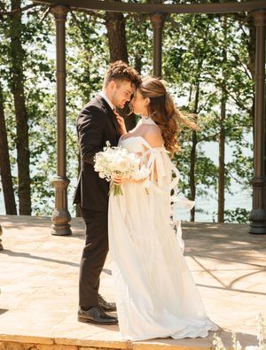 Romantic wedding moment captured in a lakeside gazebo surrounded by trees.